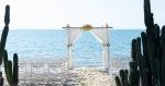 a bamboo arch covered in white gauze against the backdrop of the ocean on a beach