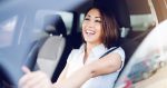 Attractive smiling caucasian brunette driving her car. Hands are on steering wheel
