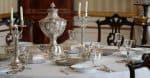 Old vintage silver tableware set out on table with white tablecloth in vintage interio