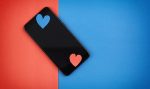 black modern smartphone with red and blue craft paper valentine hearts on color papers background, top view with flatlay copy with space on blue color, concept of modern virtual lov