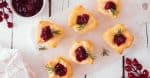 Holiday puff pastry appetizers with cranberries and baked brie. Above view serving platter against a white wood background