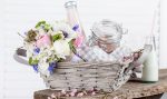 Bouquet from pink tulips, violet grape hyacinths, white anemones, violet veronica and white buttercup with violet ribbon lying in the picnic basket with milkshake in the bottle and sweets in the jar with white background and the old wooden bench