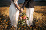 two women holding beautiful same sex wedding bouquet while doing a photoshoot on a field