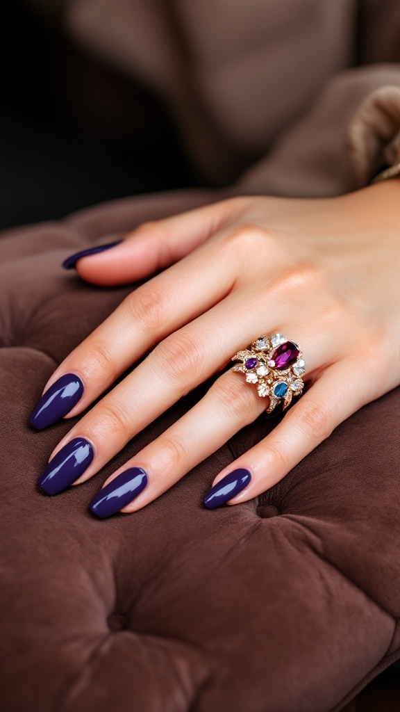 A close-up of a hand with bold purple gel nails and a jeweled ring on a plush surface.