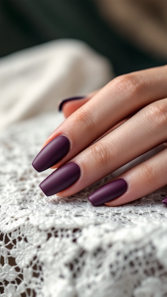 Hand with deep plum matte finish nails resting on lace fabric