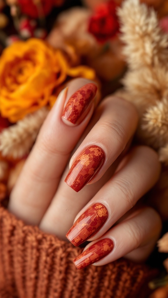 Close-up of a hand with terracotta textured nails against an autumn-themed background of flowers and foliage.