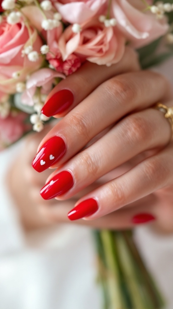 Elegant red nails with heart accents, held near a bouquet of pink flowers.