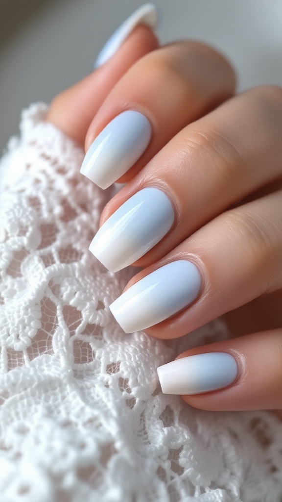 A hand with gradient light blue and white nails, placed on a soft fabric background.
