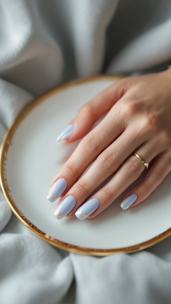 A hand with light blue wedding nails featuring gold foil details, resting on a gold-rimmed plate.