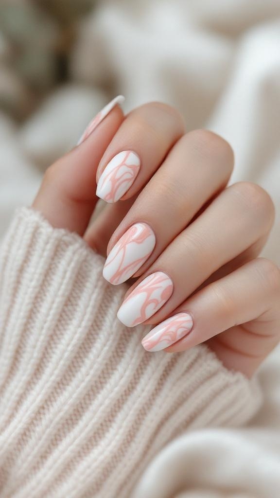 A close-up of elegant marble nail art featuring pink swirls on a white base, held against a cozy knitted sweater.