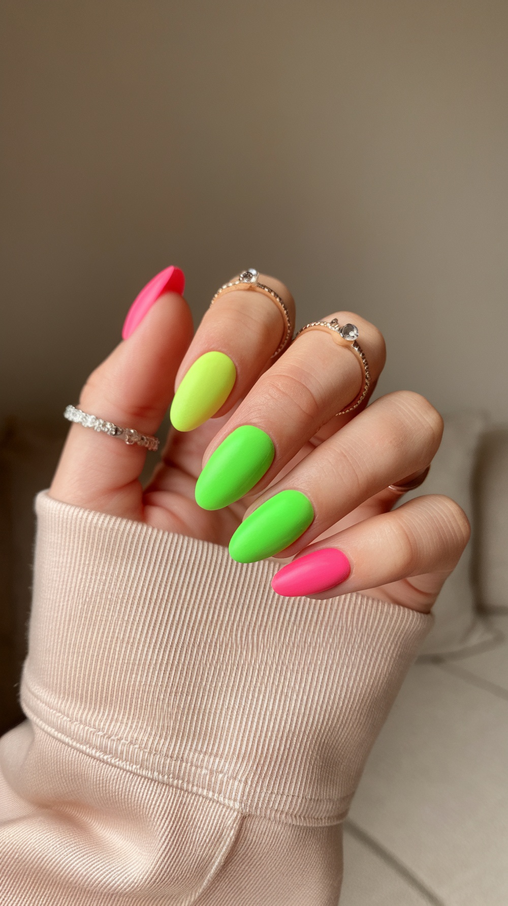 Close-up of hands with bright neon pink and green nails, showcasing a modern matte finish.