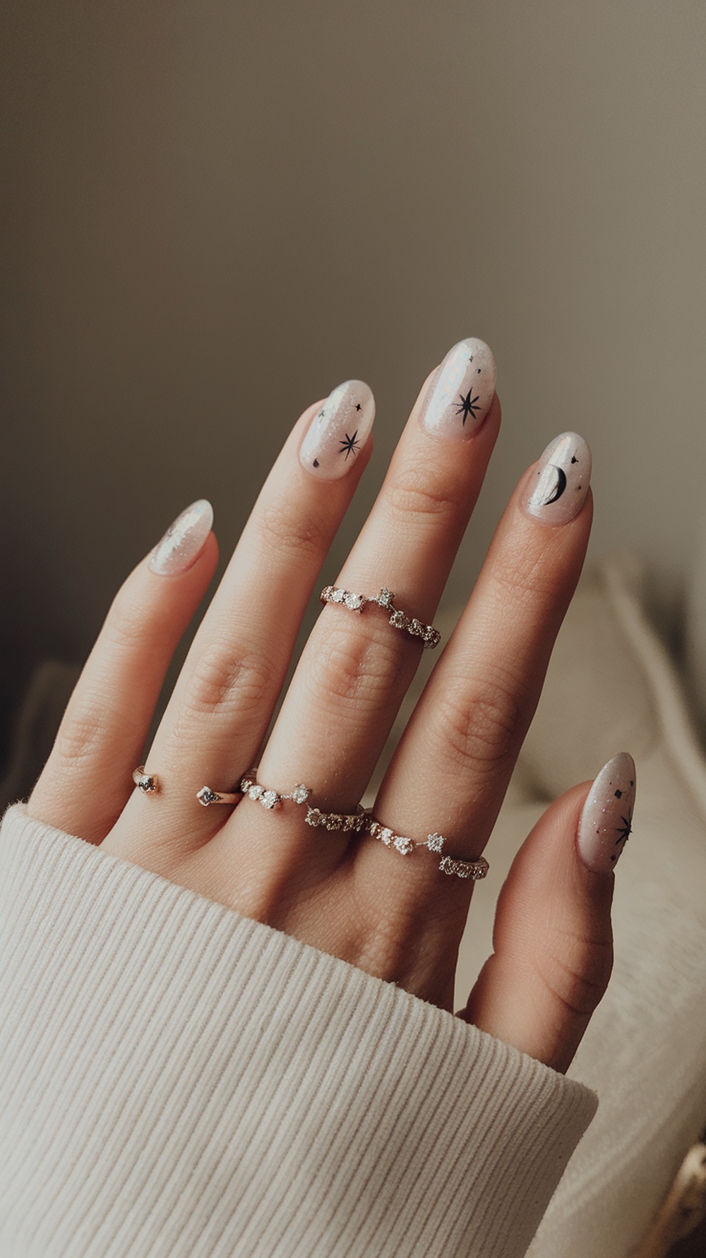 A hand with celestial-themed nail art featuring stars and a crescent moon, adorned with delicate rings.