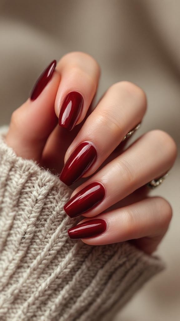Close-up of hands with dark cherry red nails, wearing a cozy knitted sweater.