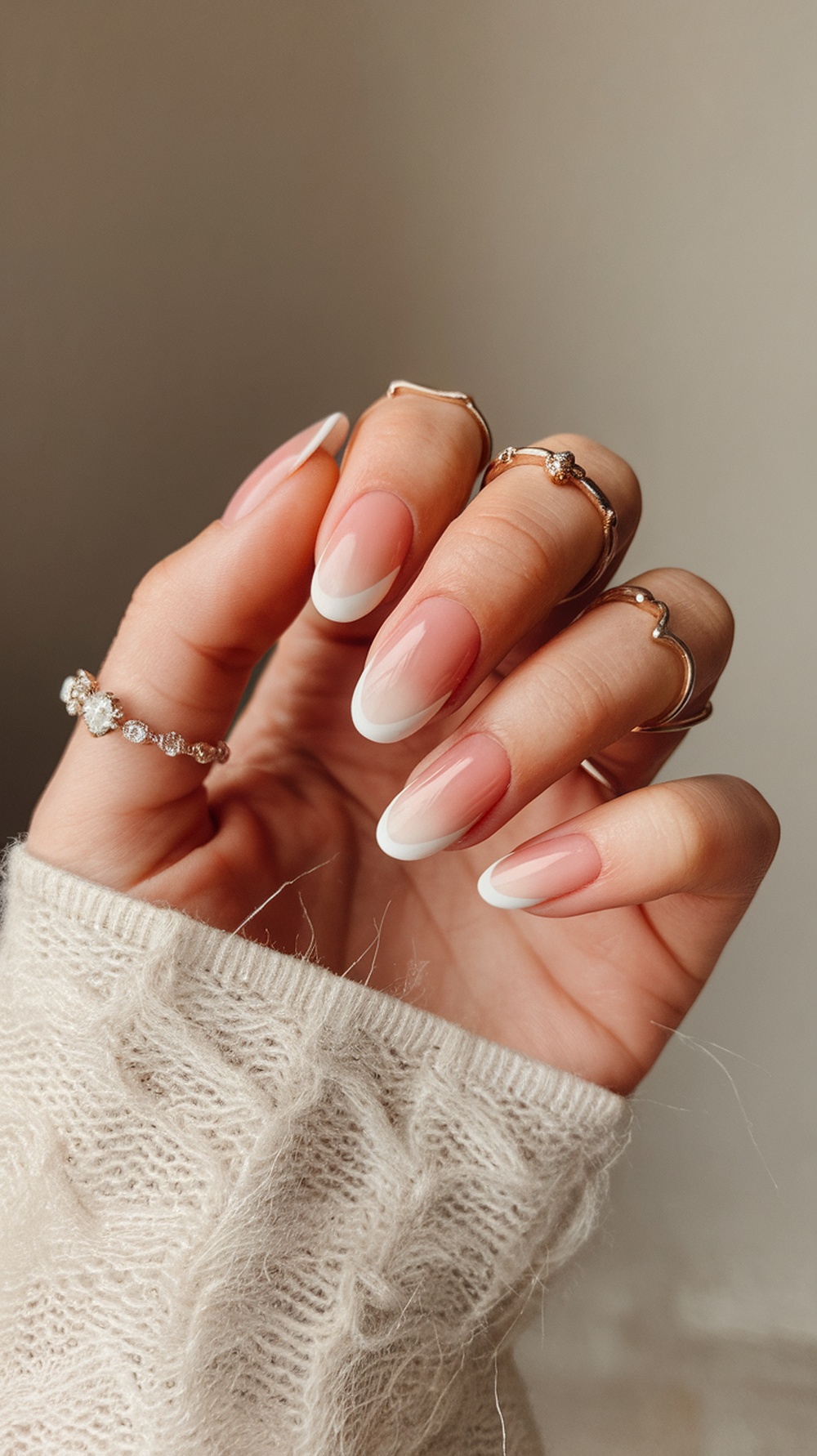 A hand showing elegant ombre nails with a soft pink base and white tips, adorned with delicate rings.