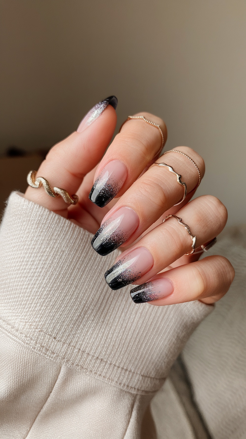 Close-up of hands with gradient glitter nails featuring pink and black colors, adorned with rings.