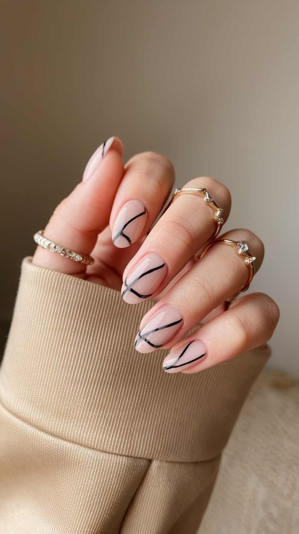 A hand with minimalist nail art featuring a nude base and black lines, adorned with rings.
