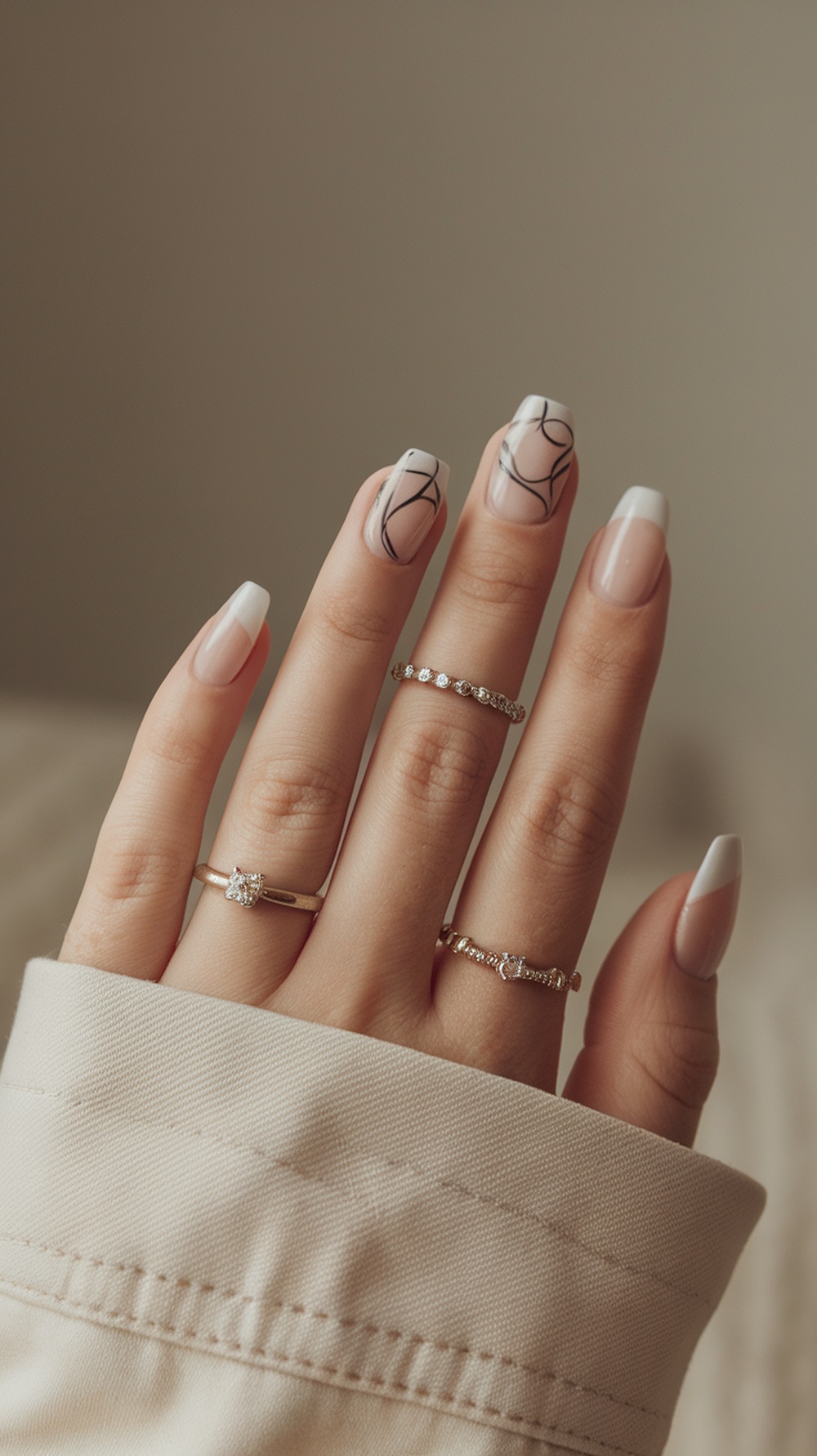Close-up of manicured nails with a mystic forest design featuring black lines on a neutral base, adorned with delicate rings.