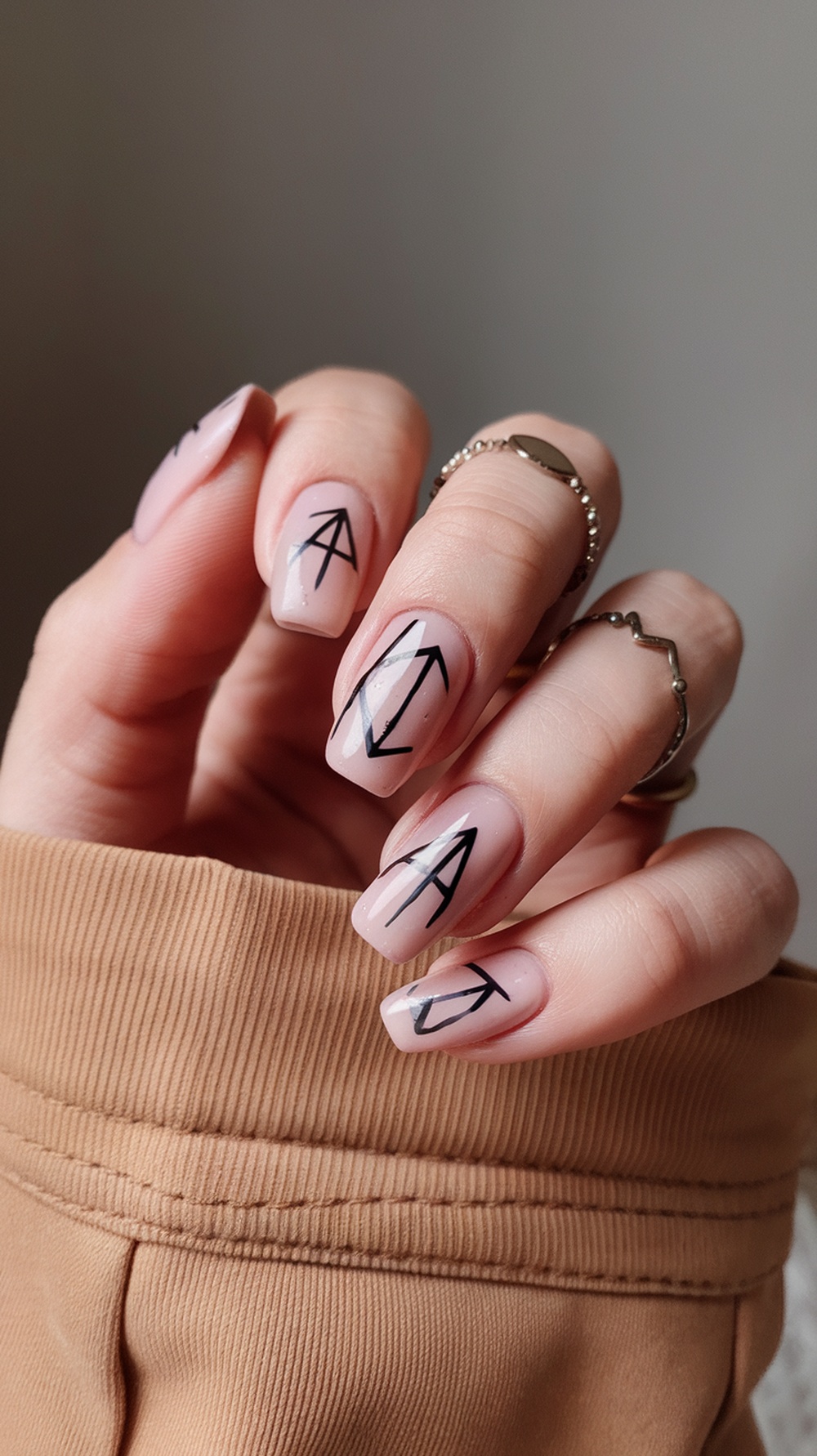 Close-up of manicured nails with black mystical symbols on a nude background