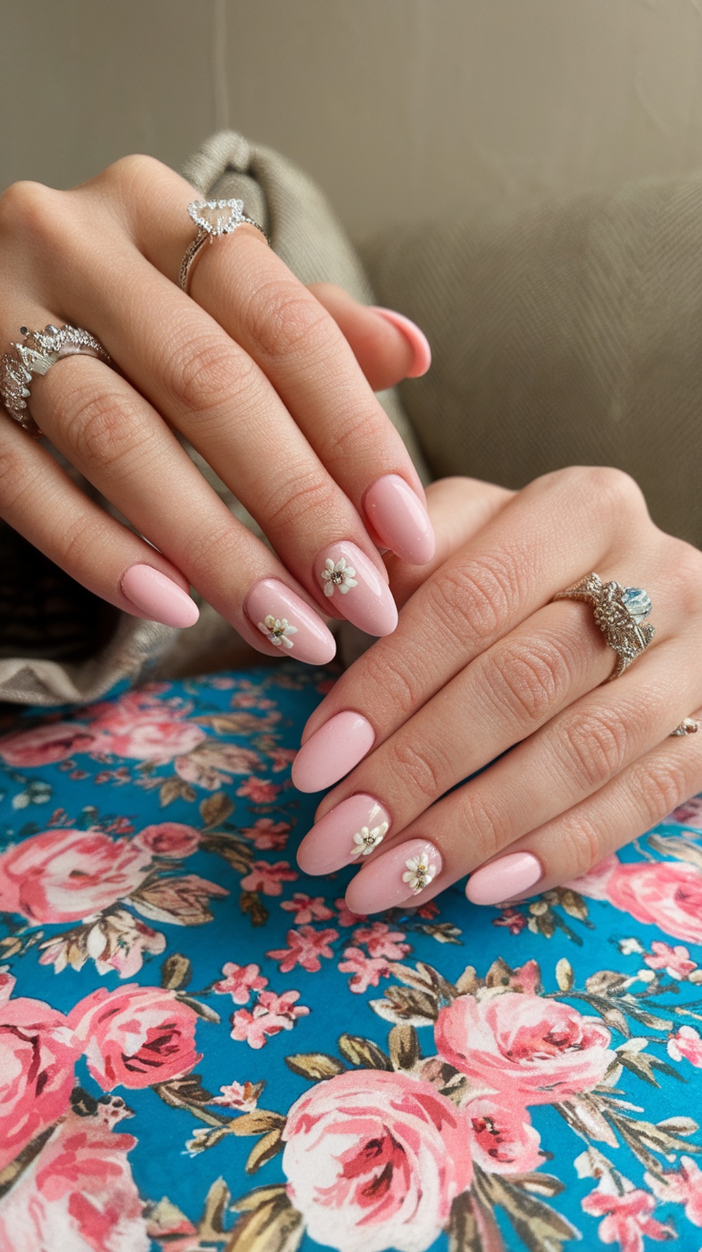 Close-up of hands with pink cat eye nails featuring floral accents, resting on a floral patterned background.