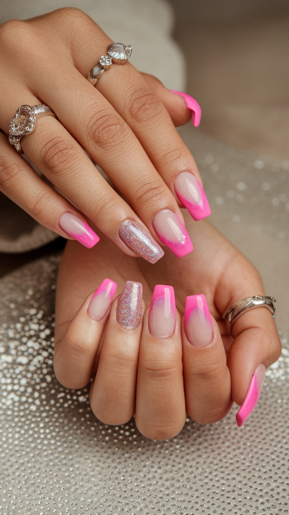 Close-up of hands with pink cat eye nails featuring glitter fade and silver rings.