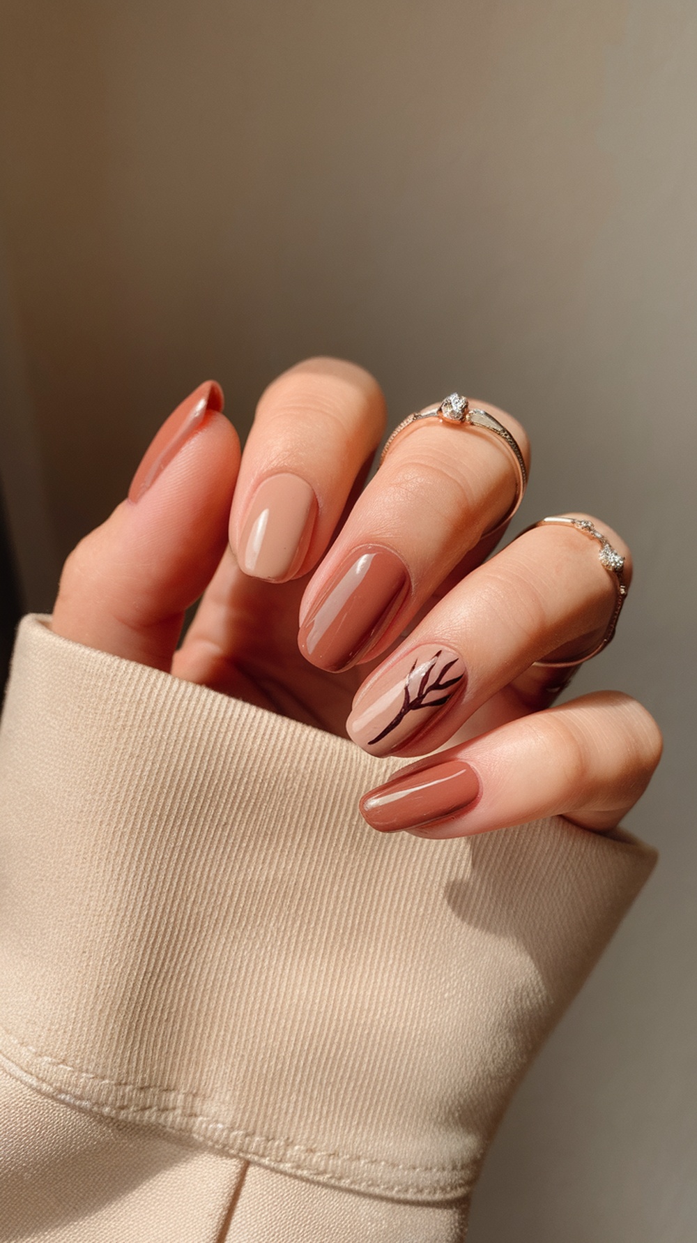 A close-up of manicured nails featuring earthy tones and a branch design.