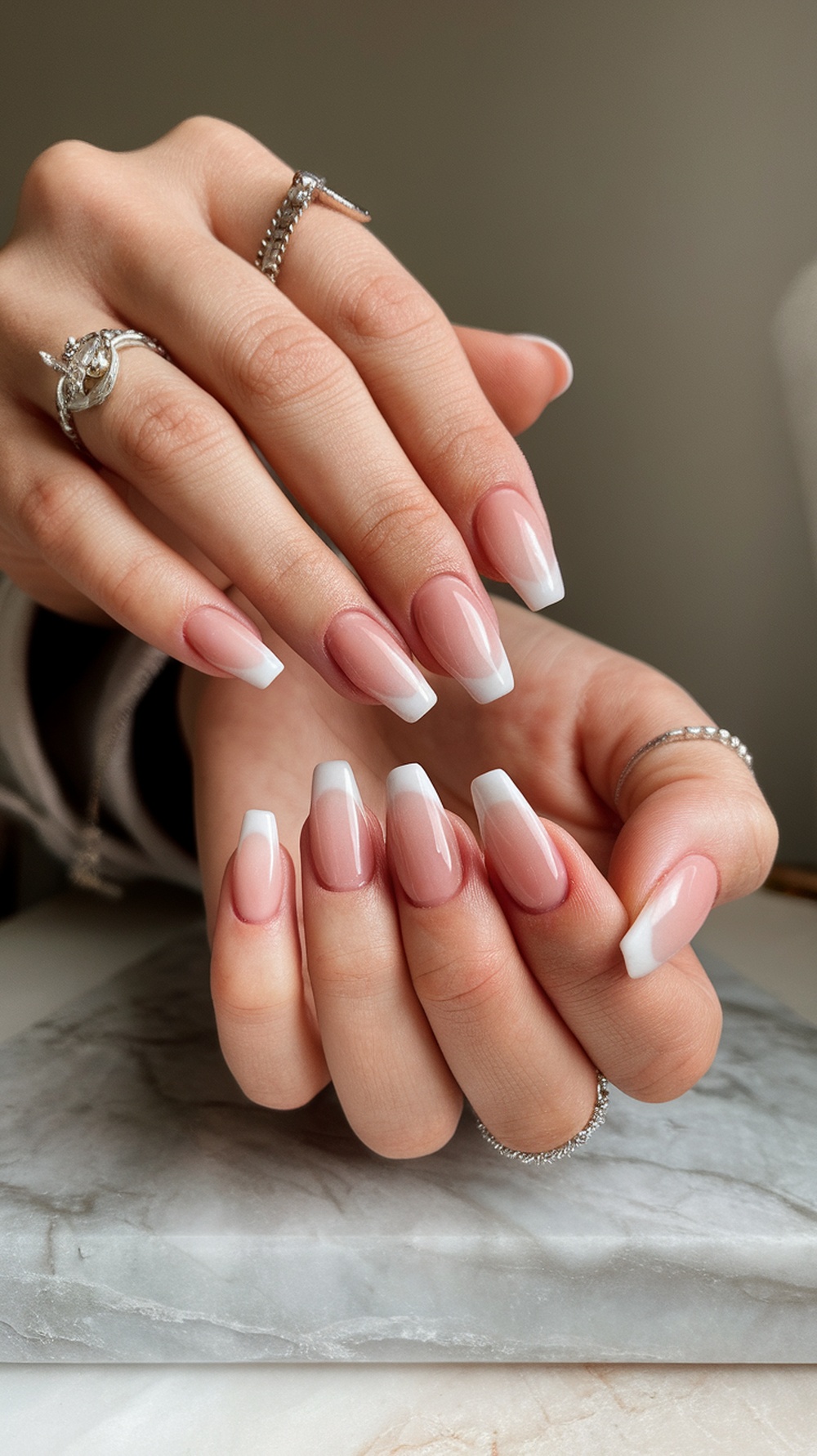 A close-up of hands with soft pink ombre cat eye nails, featuring silver rings.