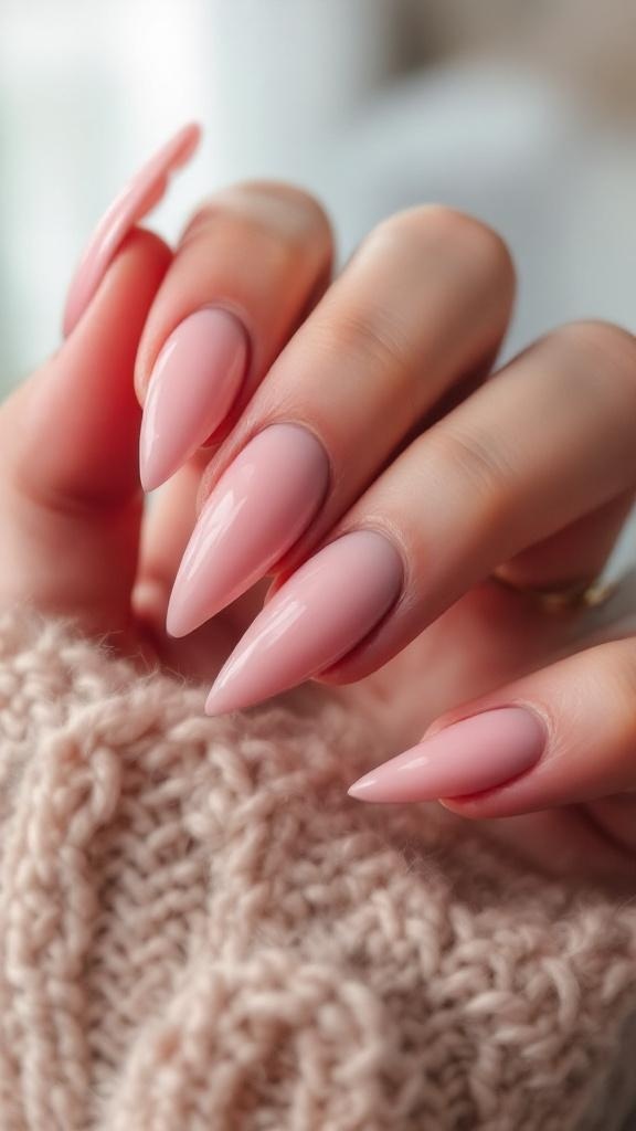 A close-up of a hand with stiletto nails, showcasing a soft pink polish, with nail care products in the background.