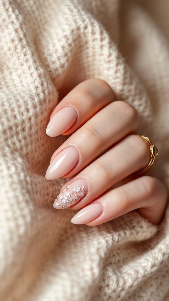 A hand with almond-shaped nude nails, featuring one nail adorned with sparkles, resting on a soft, knitted fabric.