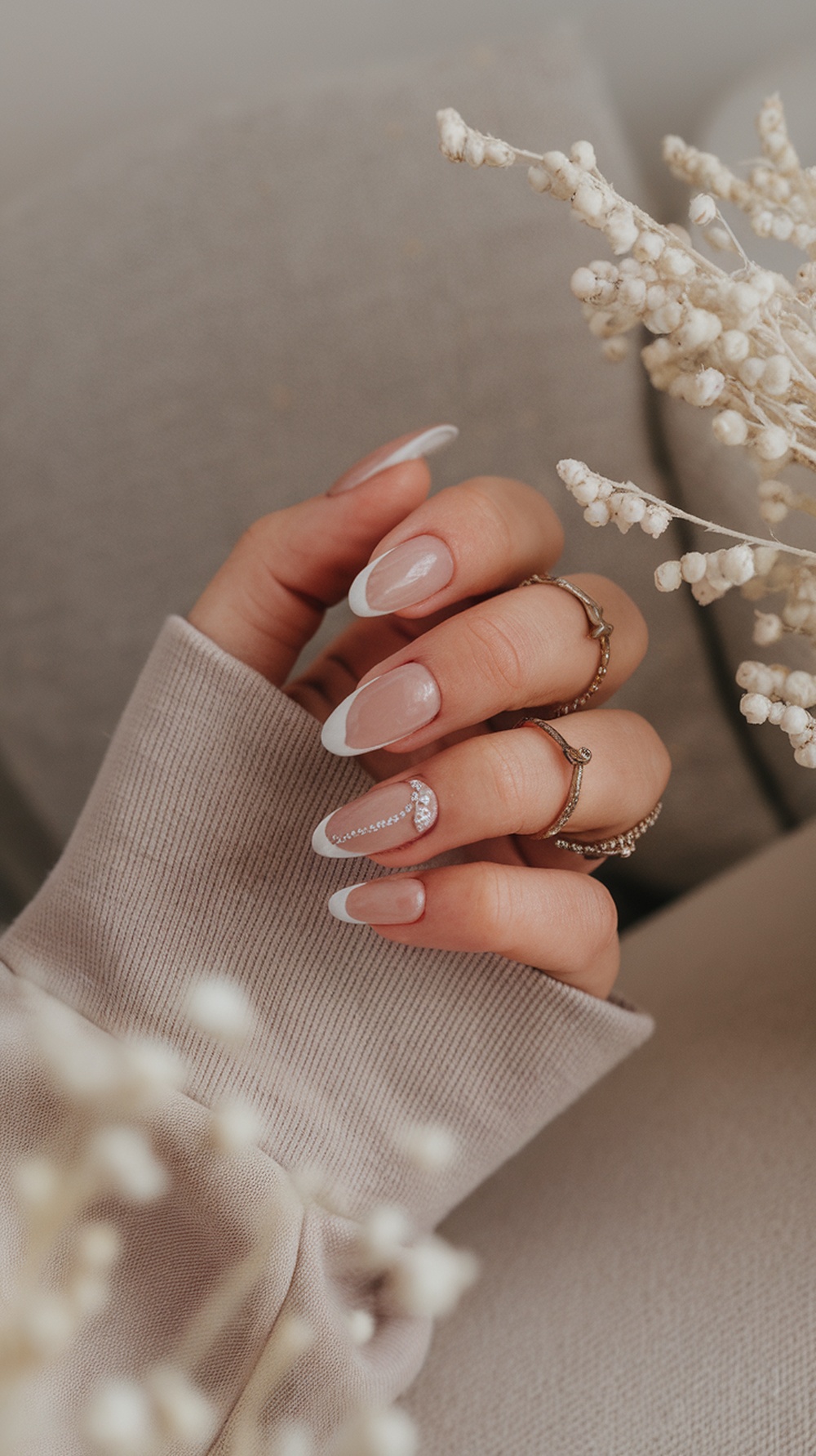 A close-up of elegantly manicured bridal nails featuring nude and white tips, adorned with a sparkling design, complemented by delicate rings.