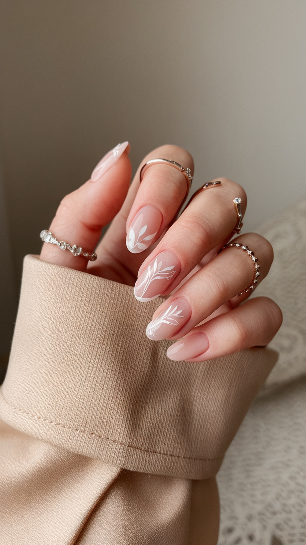 Elegant bridal nails with red polish and white floral accents, showcasing delicate rings.