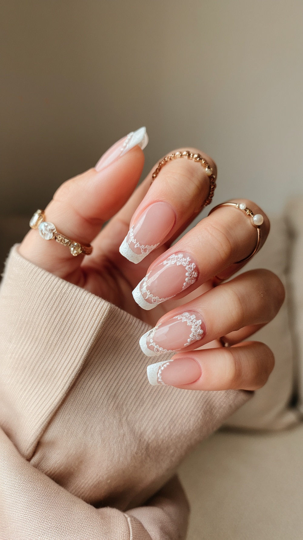 A close-up of elegant bridal nails featuring French tips with lace detailing, complemented by delicate rings.